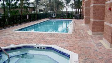 Una piscina con solárium empedrado y un jacuzzi.