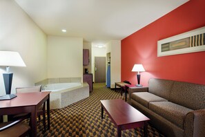 A hotel room with a bed, a sitting area with a sofa and a table, a small table with a lamp, and a bathroom with a bathtub and a shower. - Holiday Inn Express Hotel & Suites Malvern by IHG (Malvern)