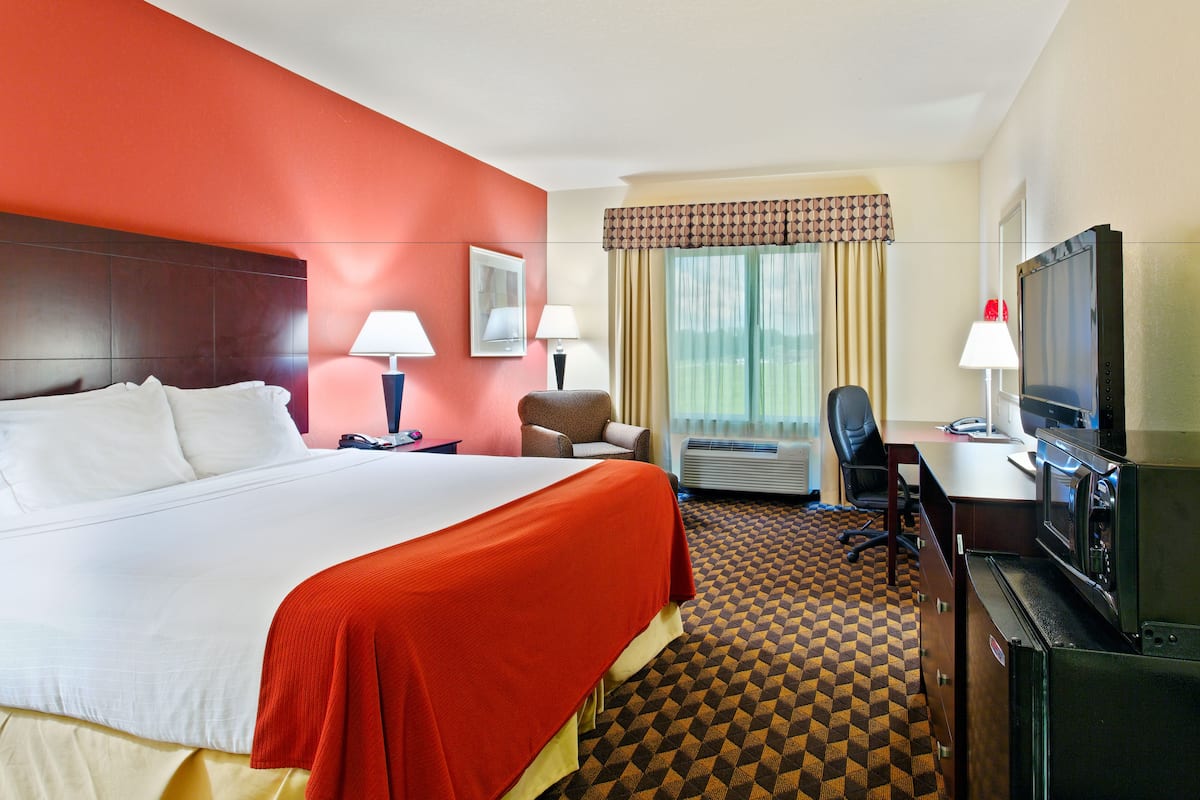A hotel room with a large bed, a desk with a computer, a TV, and a chair.