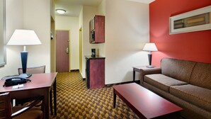 Una habitación de hotel con una mesa de comedor, dos sillas, un sofá, un armario pequeño y una lámpara.