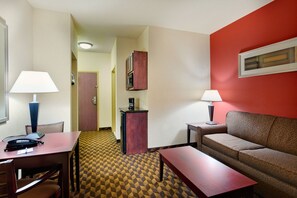 A hotel room with a dining table, two chairs, a sofa, a small cabinet, and a lamp. - Holiday Inn Express Hotel & Suites Malvern by IHG (Malvern)