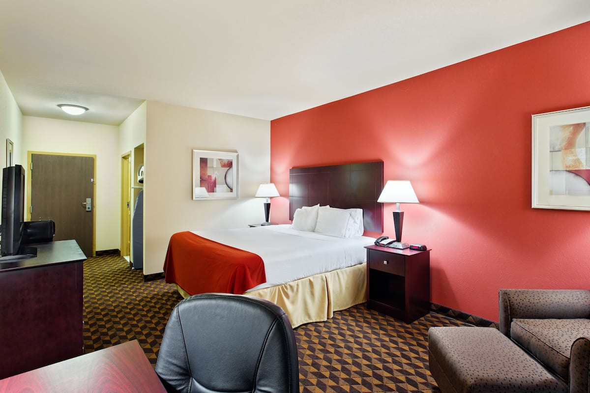 A hotel room with a bed, a desk, a chair, a nightstand, and a lamp.