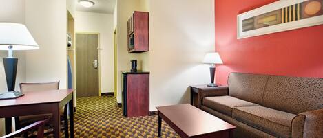 Une chambre d’hôtel avec une moquette à motifs, un canapé, une table, un bureau avec une lampe et un placard.