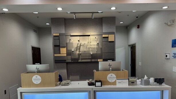 Un espace d’accueil d’hôtel au design moderne, comprenant un comptoir d’accueil doté d’un écran numérique, une enseigne pour le Holiday Inn Express Suites et un terminal d’enregistrement.