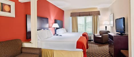 A hotel room with a large bed, a sofa, a desk with a TV, and a window with curtains.