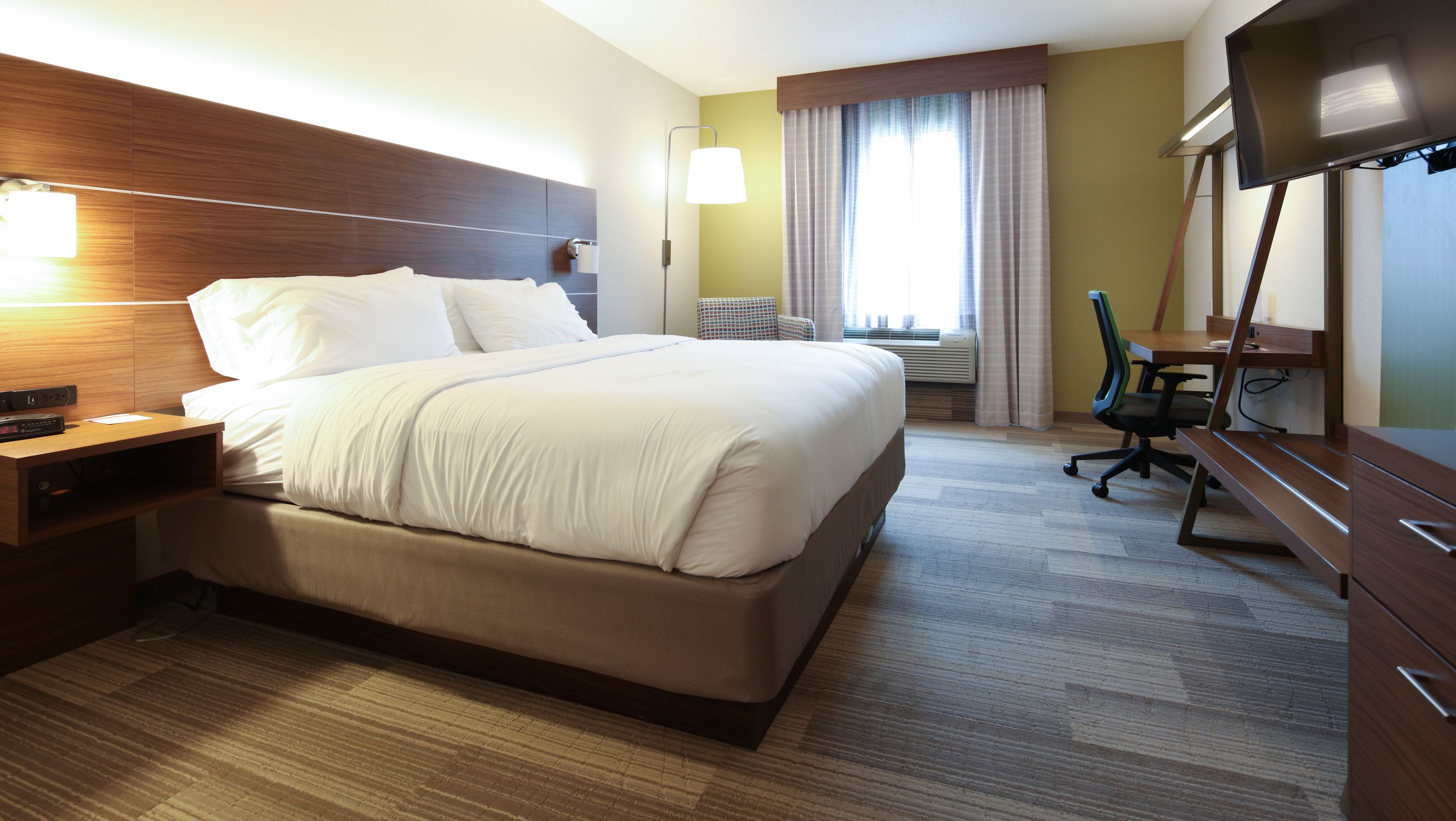 Habitació d'hotel amb un llit gran, escriptori amb cadira, televisió de pantalla plana i finestra amb cortines.