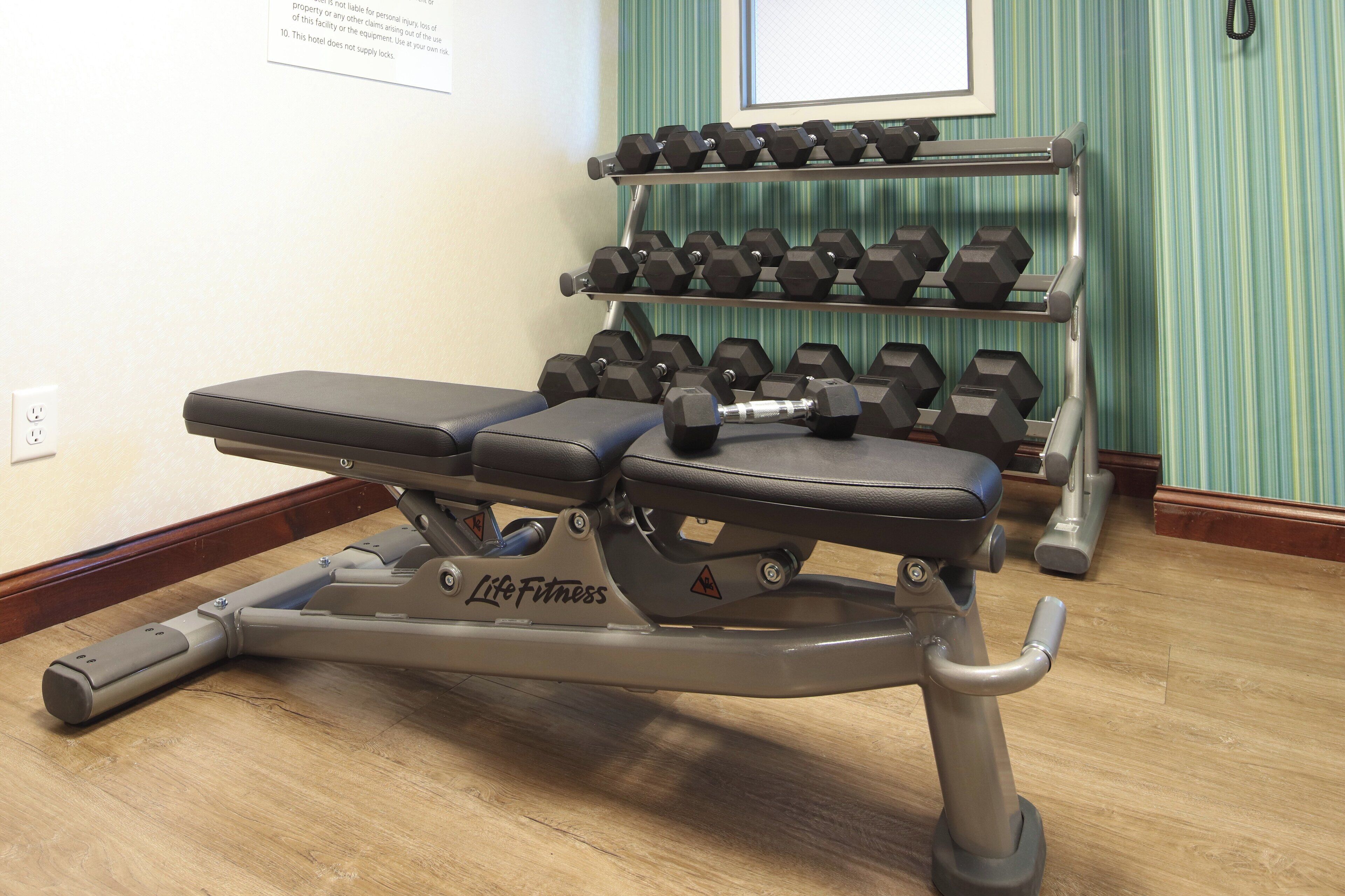 Un gimnasio con una prensa de banca, mancuernas y una cinta de correr.