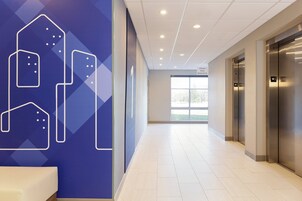 Corredor moderno de hotel com parede azul com formas geométricas, um banco branco e um elevador.