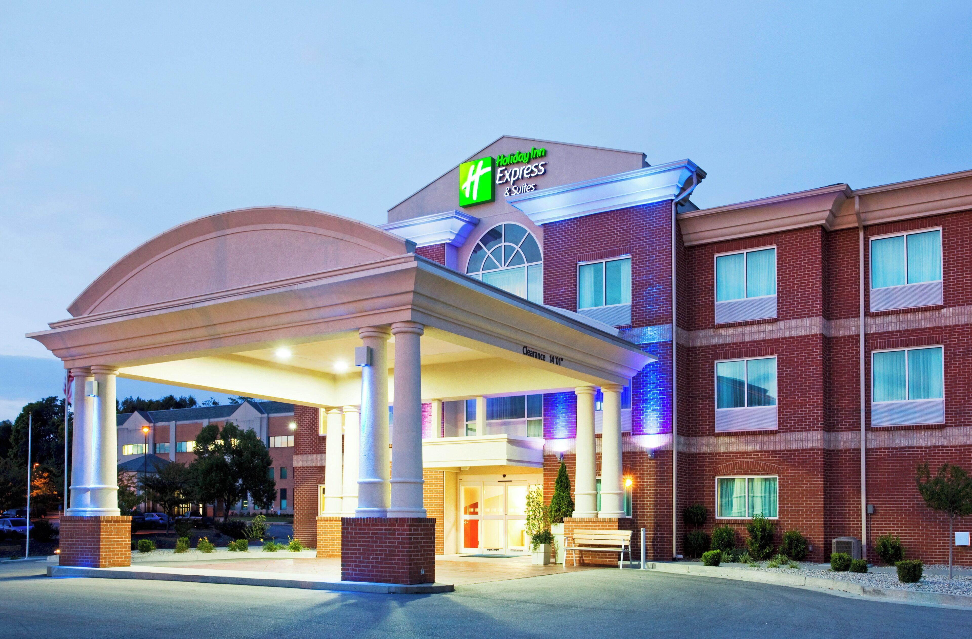 A Holiday Inn Express & Suites with a covered entrance, brick facade, and a clear sky.