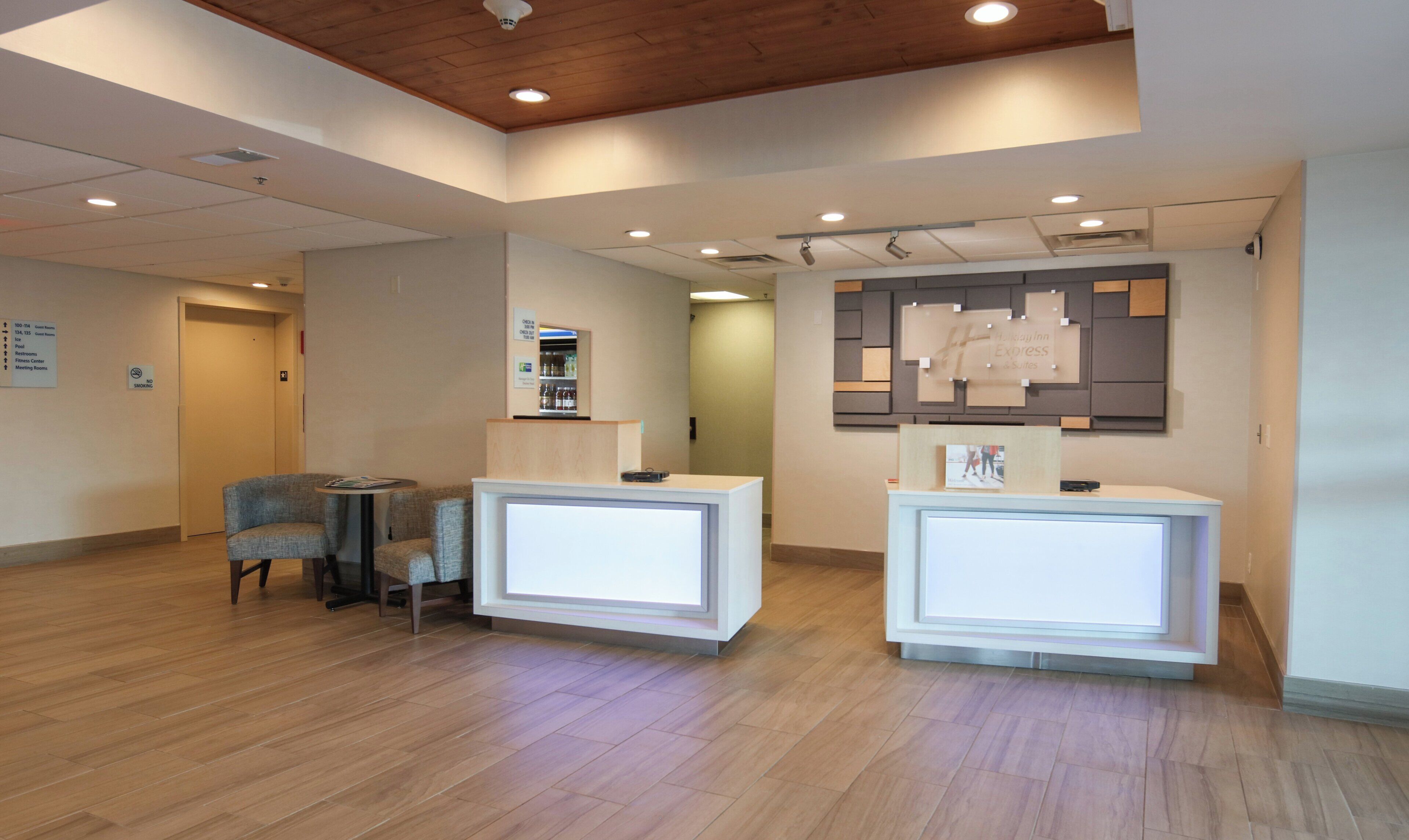 A reception area with two reception desks, a seating area with chairs, and a wall-mounted display.