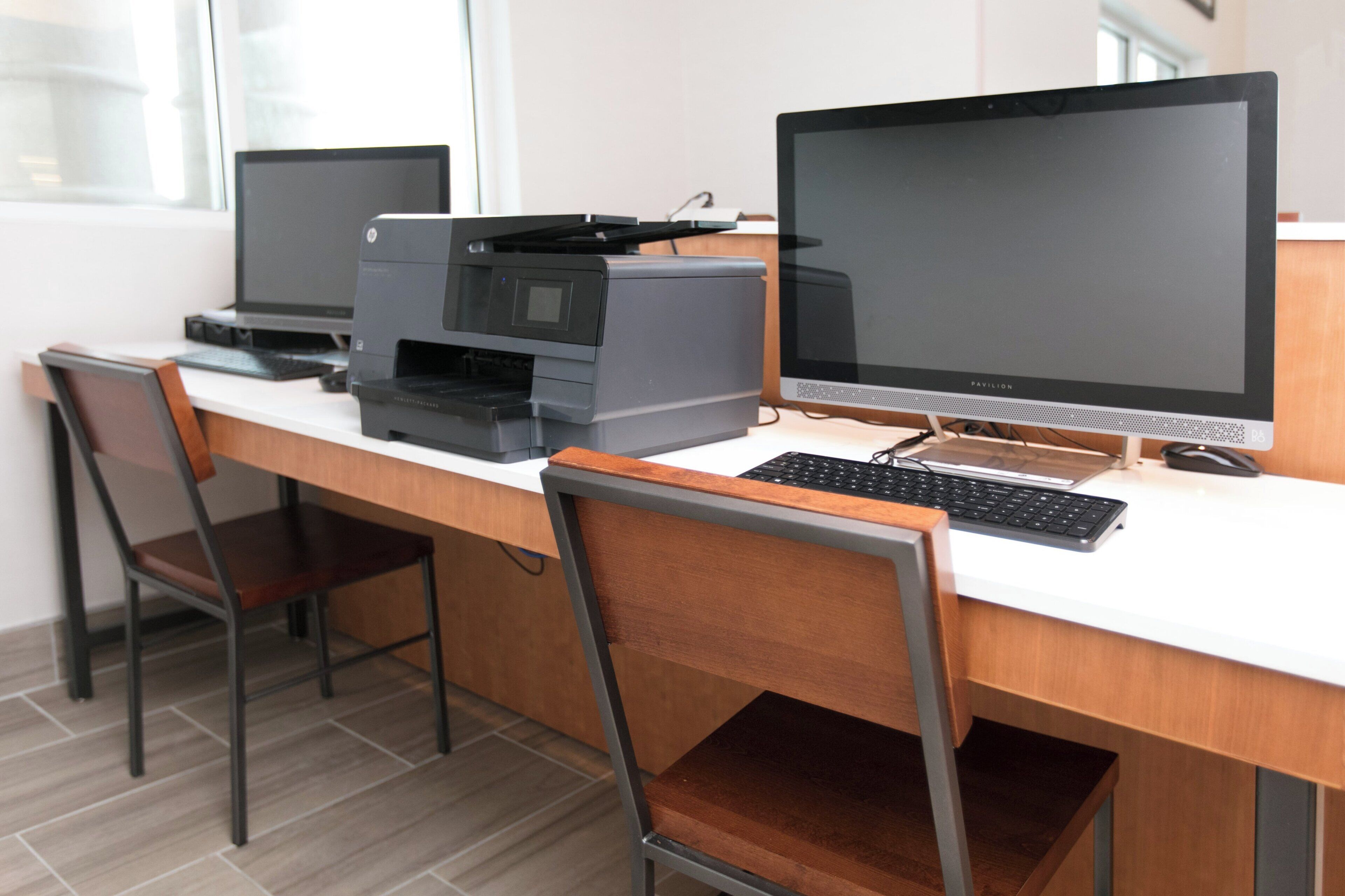 A workspace with two desktop computers, a printer, and a keyboard on a white desk.