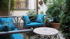 Un espace extérieur aménagé avec une table et des chaises en métal, un pot de fleurs et une fenêtre ornée de barreaux en métal.