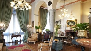 Un salon spacieux agrémenté d’un grand lustre, de rideaux verts et de divers meubles, notamment un canapé, des fauteuils et une table basse.