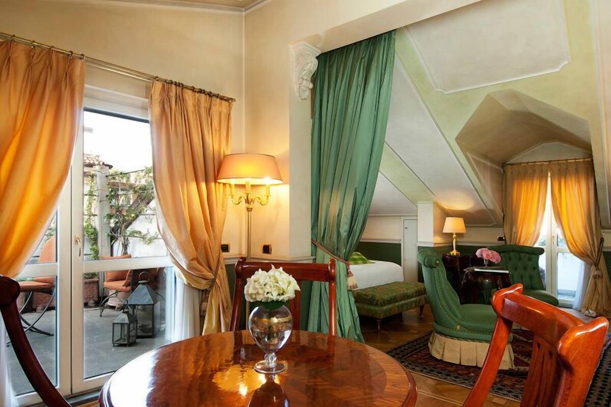 Een hotelkamer met een eettafel, een groene fauteuil, een bank en een bed.
