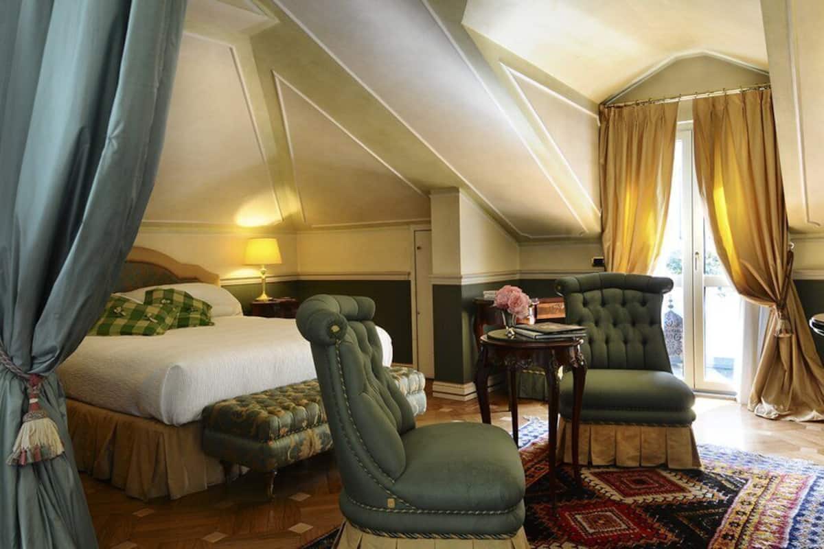 Een slaapkamer met een bed, een groene fauteuil, een kleine tafel en een kamerkleed met dessin.