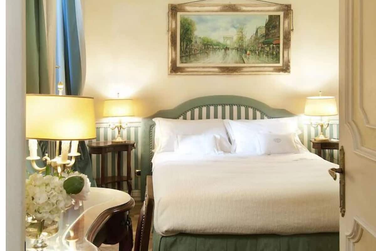 Een hotelkamer met een bed, twee bedlampen, een schilderij aan de muur en een spiegel met gordijnen.