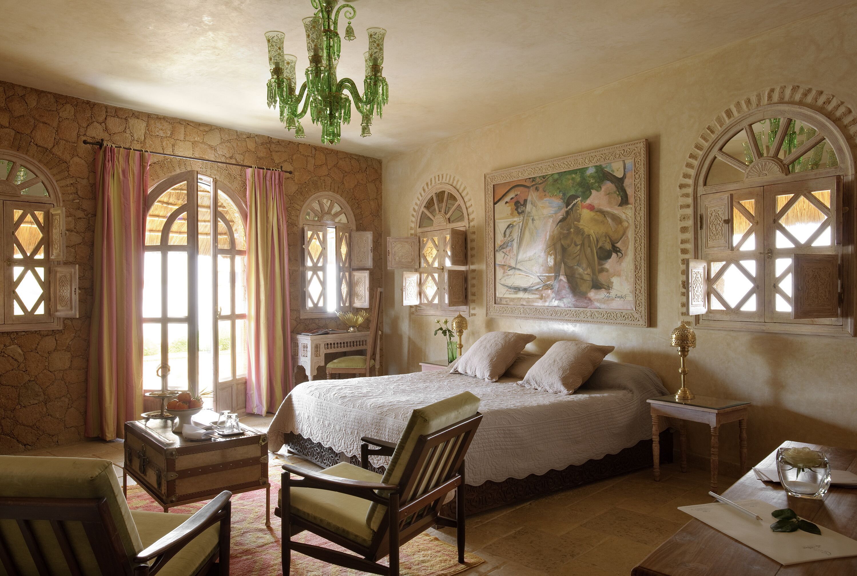 A bedroom with a large bed, a wooden chair, a desk, and a chandelier.