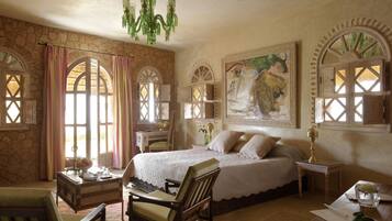 A bedroom with a large bed, a wooden chair, a desk, and a chandelier.