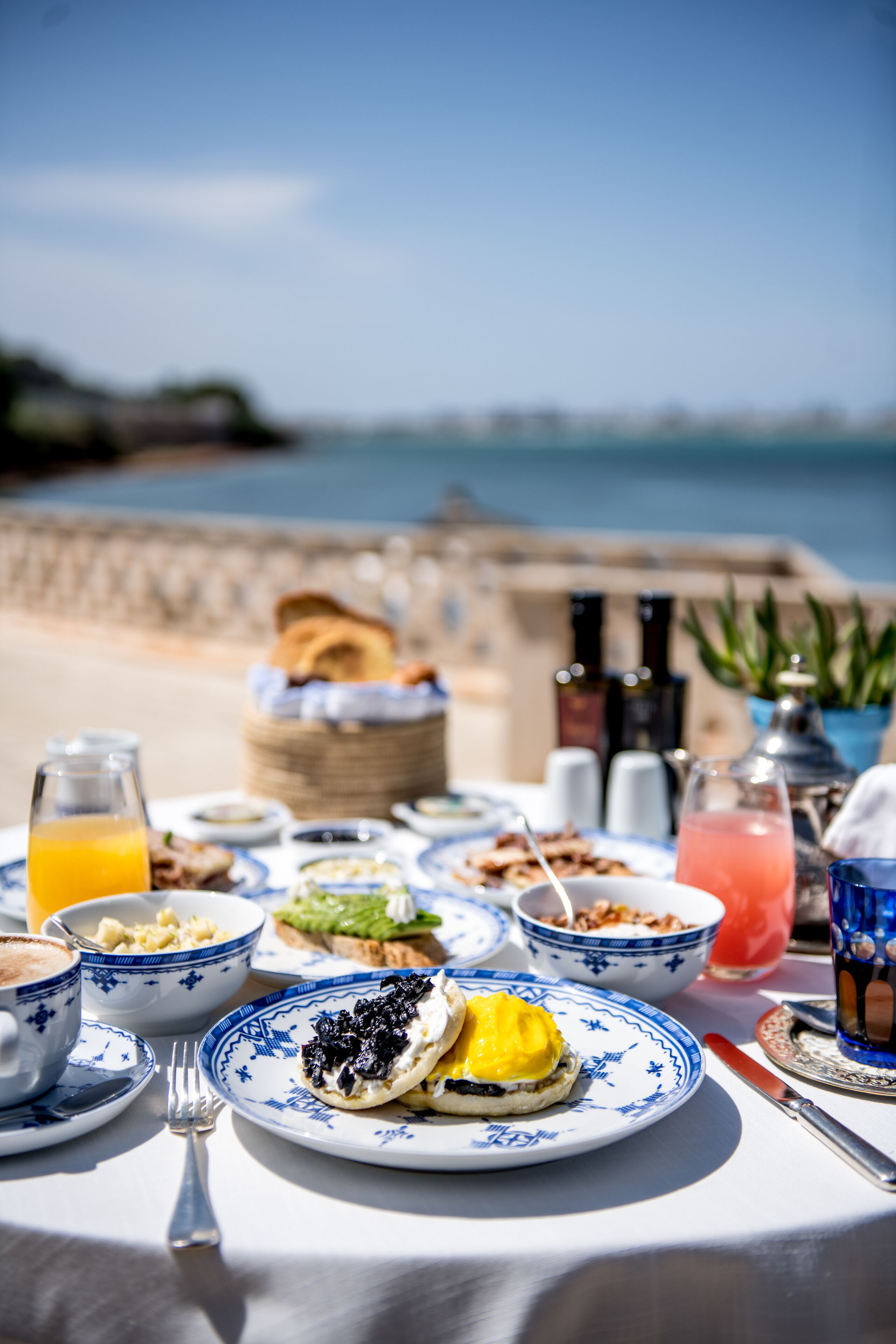 A table set with breakfast items including eggs, toast, and beverages, overlooking a scenic coastal view.