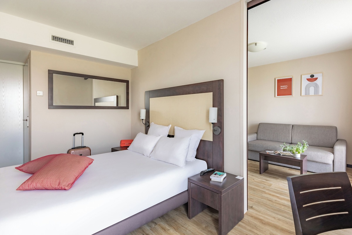 A hotel room with a large bed, a bedside table, a nightstand, a sofa, and a coffee table.