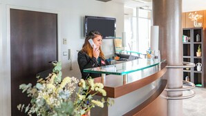 A reception desk with a glass top, a television mounted on the wall, and a large pillar.