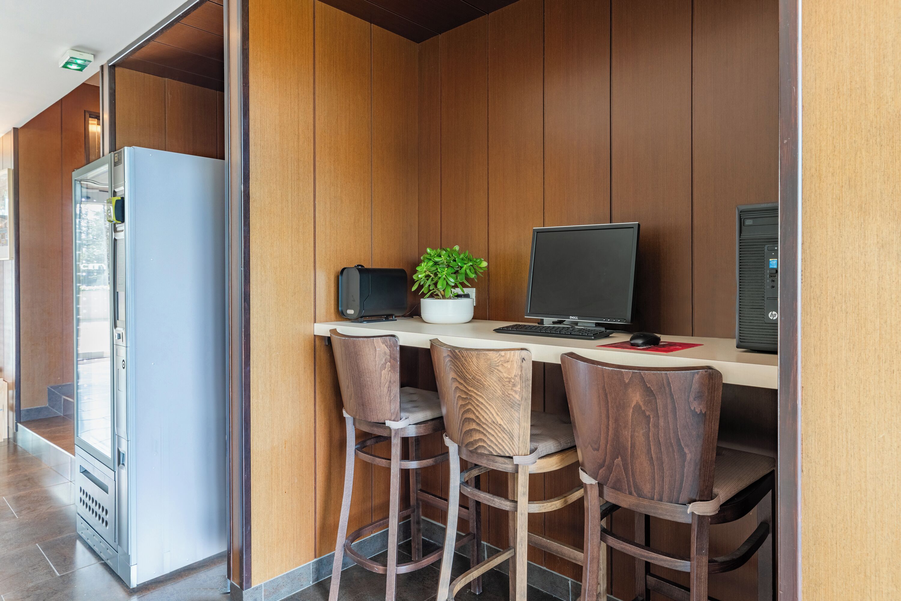 A modern workspace with a wooden desk, a laptop, a plant, and two bar stools.