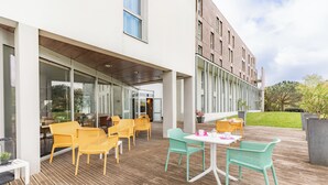 An outdoor patio with yellow and green chairs, a white table, and a glass-enclosed area.