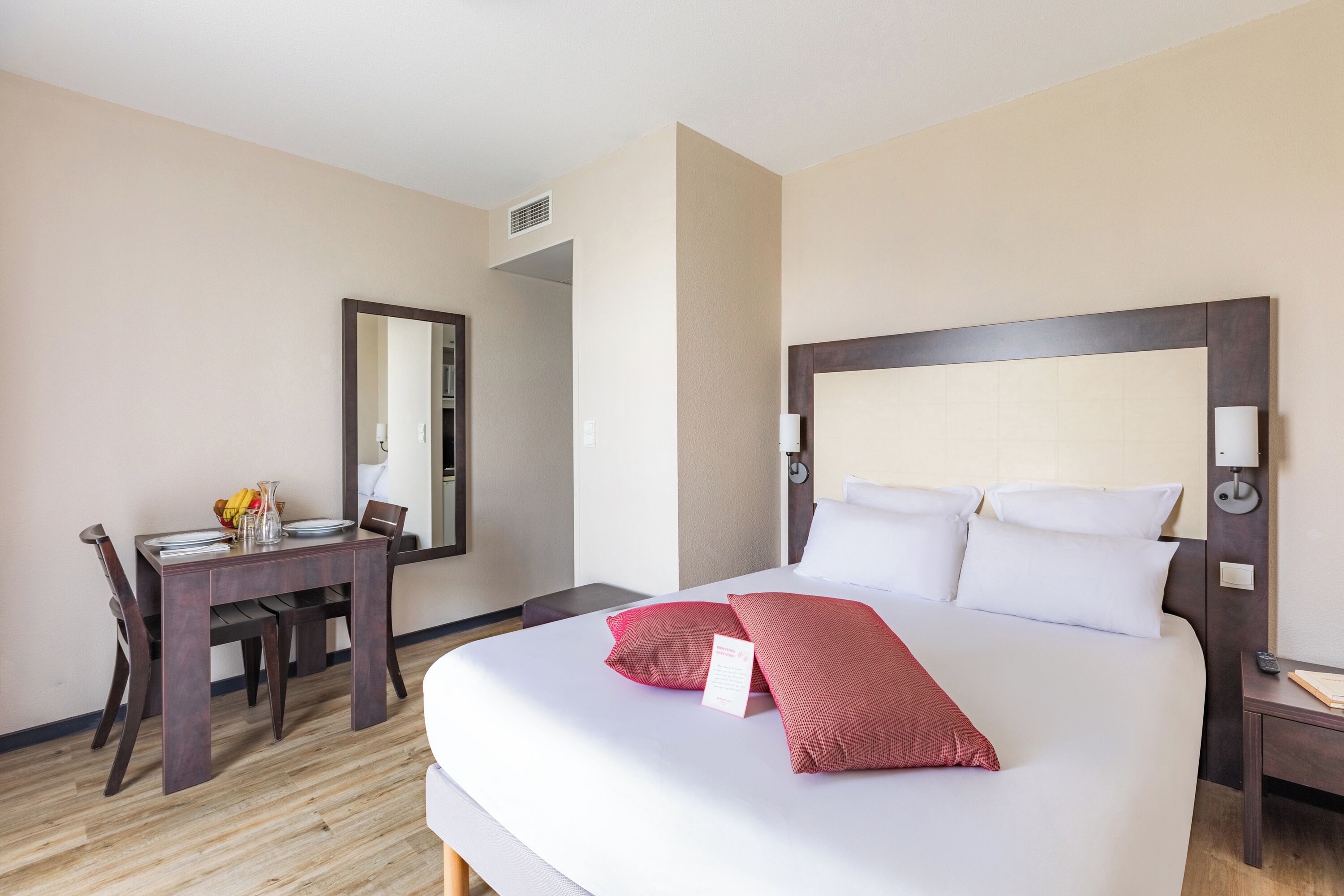 A hotel room with a large bed, a desk with a chair, and a mirror on the wall.