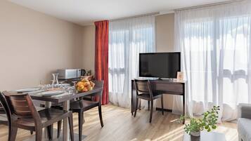 A modern hotel room with a dining area, a flat-screen TV, a sofa, and a potted plant.