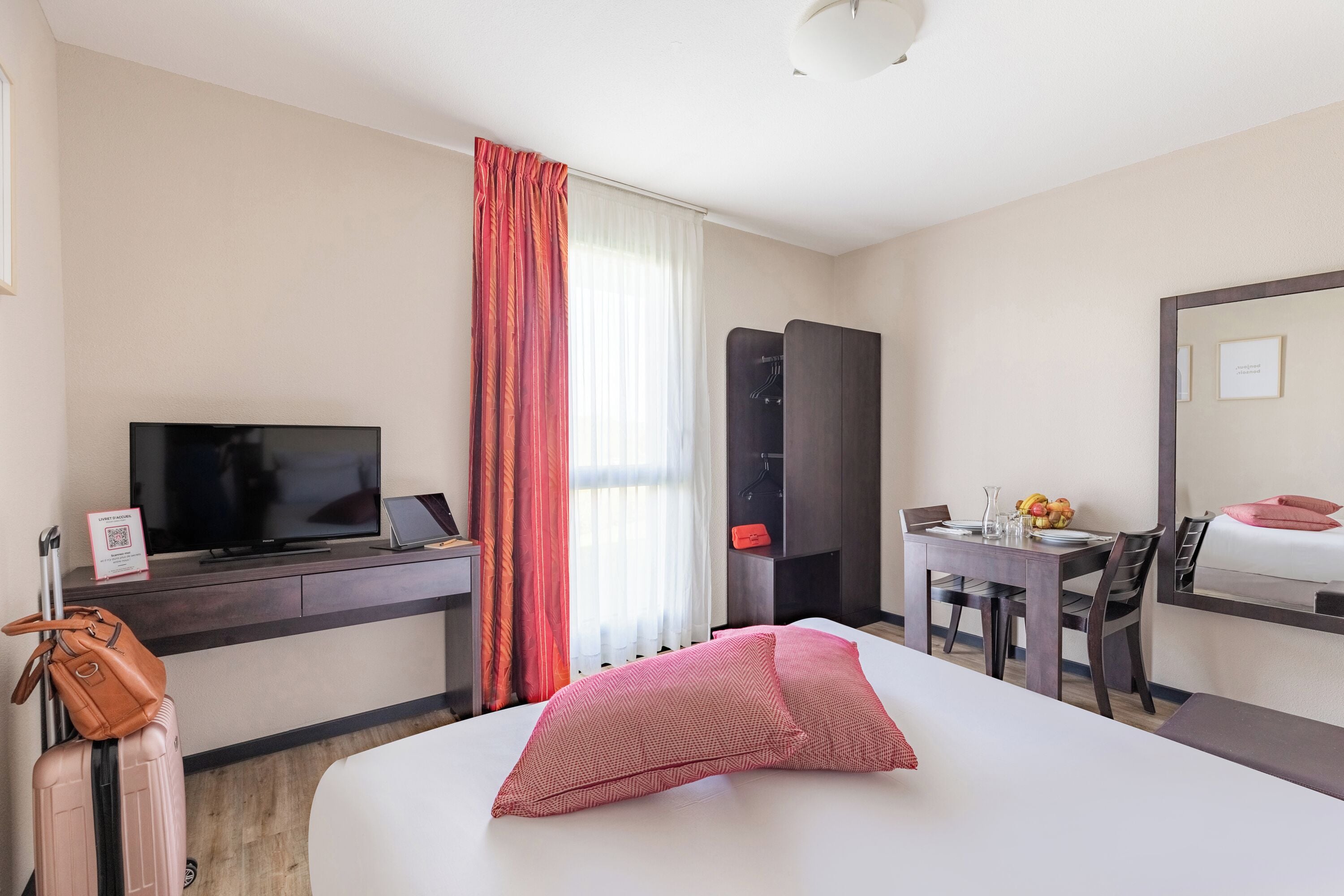 Una habitación de hotel con cama, escritorio con computadora, televisión, armario y zona de comedor con mesa y sillas.