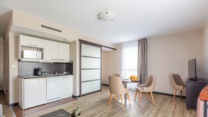 A modern hotel room with a kitchenette, dining area, and a seating space.