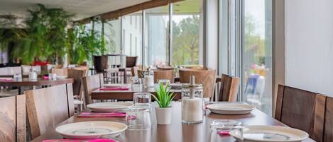 A restaurant with wooden tables and chairs, clear glassware, and potted plants.
