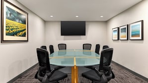 A conference room with a glass table, black chairs, a flat-screen TV, and framed pictures on the walls.