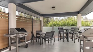 An outdoor patio area with a grill, tables, and chairs.