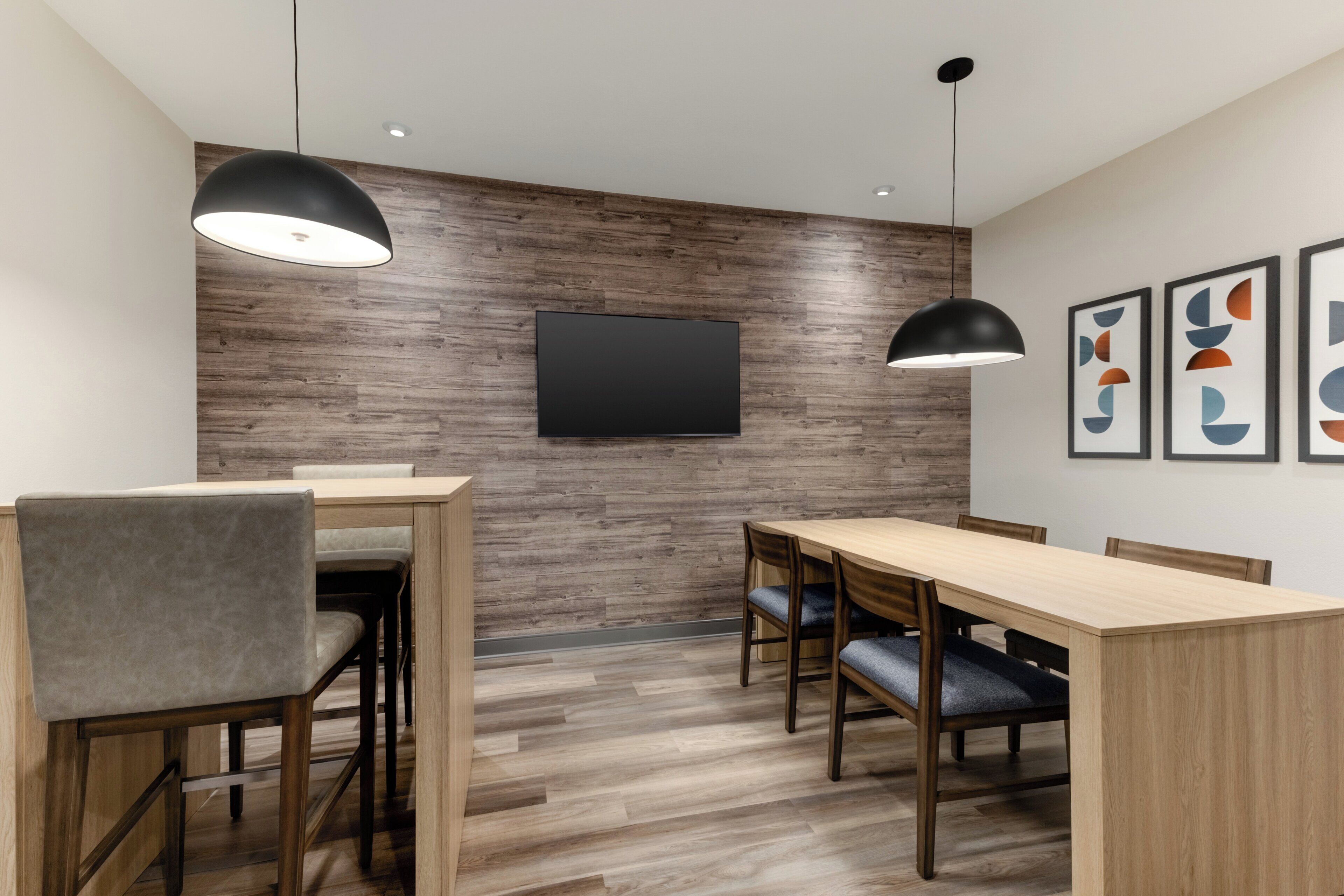 A modern meeting room with a wooden wall, a flat-screen TV, and a long table with chairs.