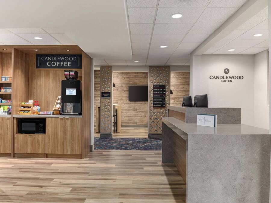 A hotel reception area with a coffee station, a reception desk, and a wall-mounted sign for Candlewood Suites.