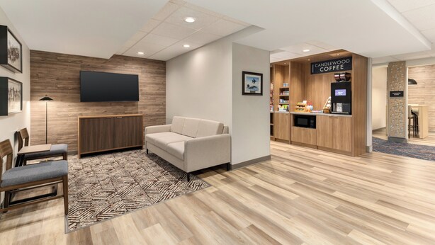 A modern hotel lobby with a seating area, a flat-screen TV, a coffee station, and a reception desk.