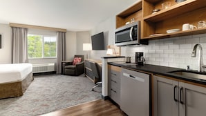 A hotel room with a bed, a desk, a chair, a kitchenette with a microwave, and a TV.