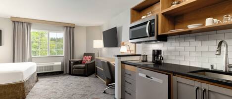 Hotelkamer met een bed, een bureau, een stoel, een kitchenette met een magnetron, en een televisie.