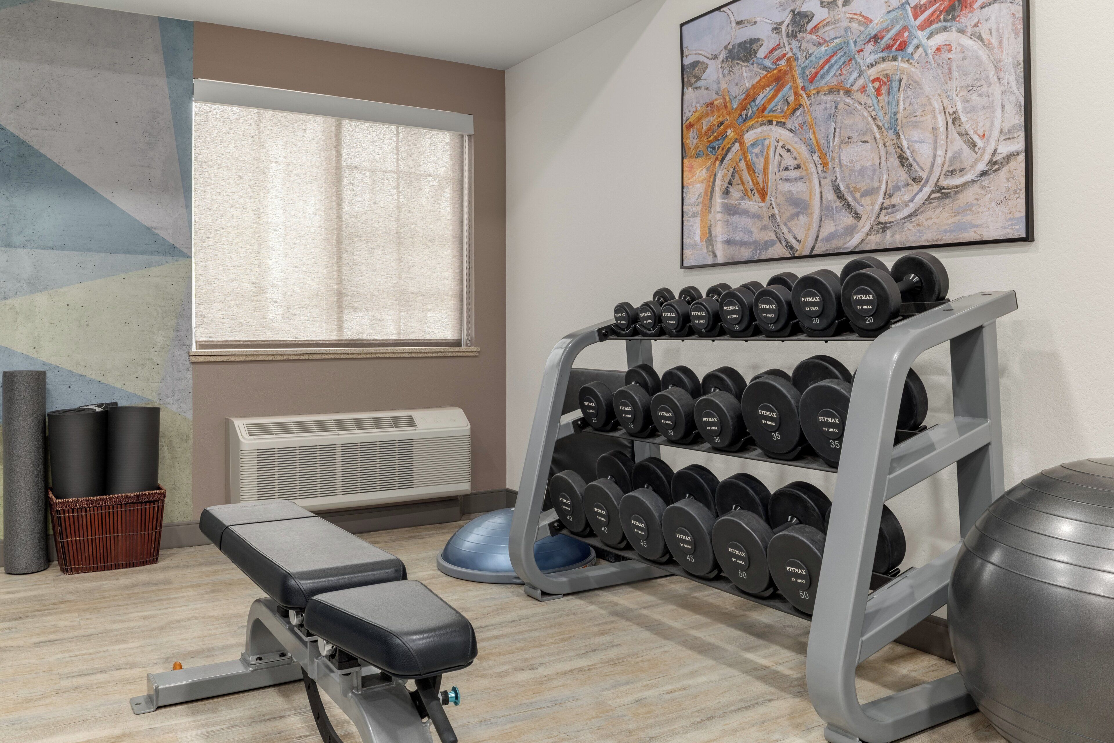 Een sportschool met een bank, gewichtsschijven, een hometrainer en een wandairconditioning.