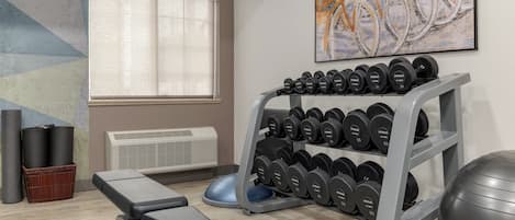 Een sportschool met een bank, gewichtsschijven, een hometrainer en een wandairconditioning.