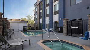 A hotel with a swimming pool, lounge chairs, and a covered patio area.