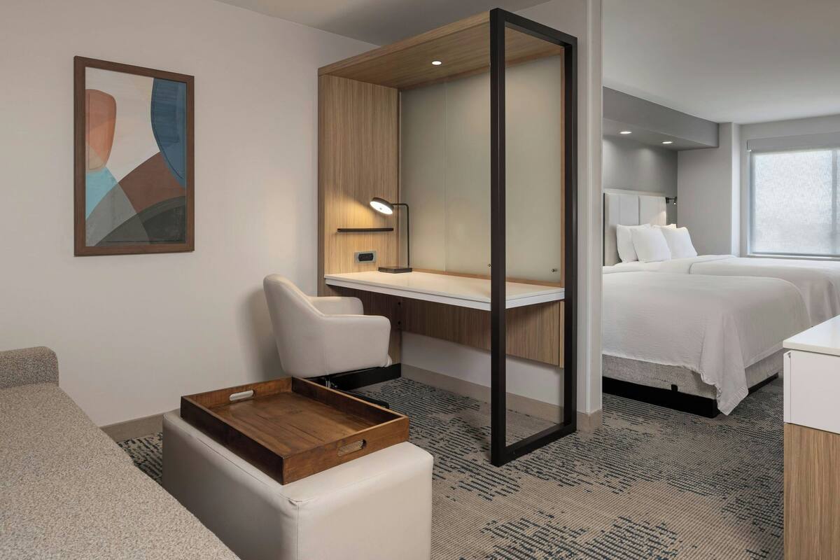 Une chambre d’hôtel moderne équipée d’un bureau, de deux lits, d’un canapé et d’une table d’appoint en bois.
