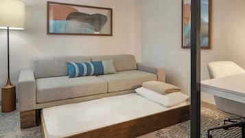 A modern hotel room with a sofa, a single bed, a desk, and a chair.