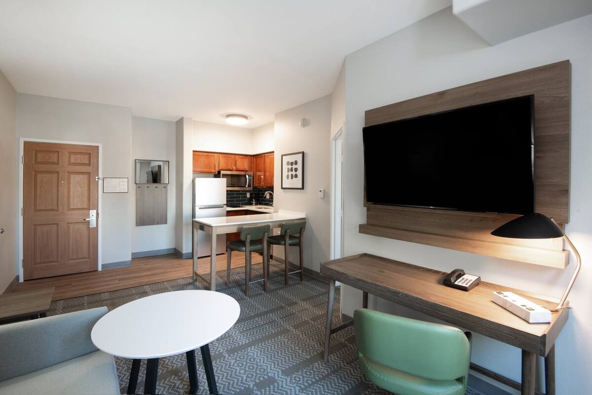 A compact living space with a kitchenette, a dining area, and a workspace with a TV and desk lamp.