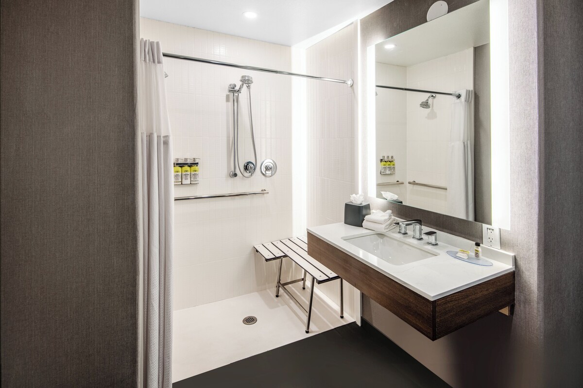 A modern bathroom with a shower, a bench, a sink, and a large mirror.