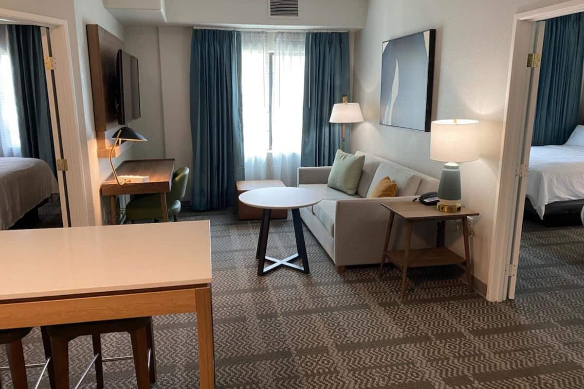 A hotel room with a bed, a sofa, a small table, a desk, and a chair.