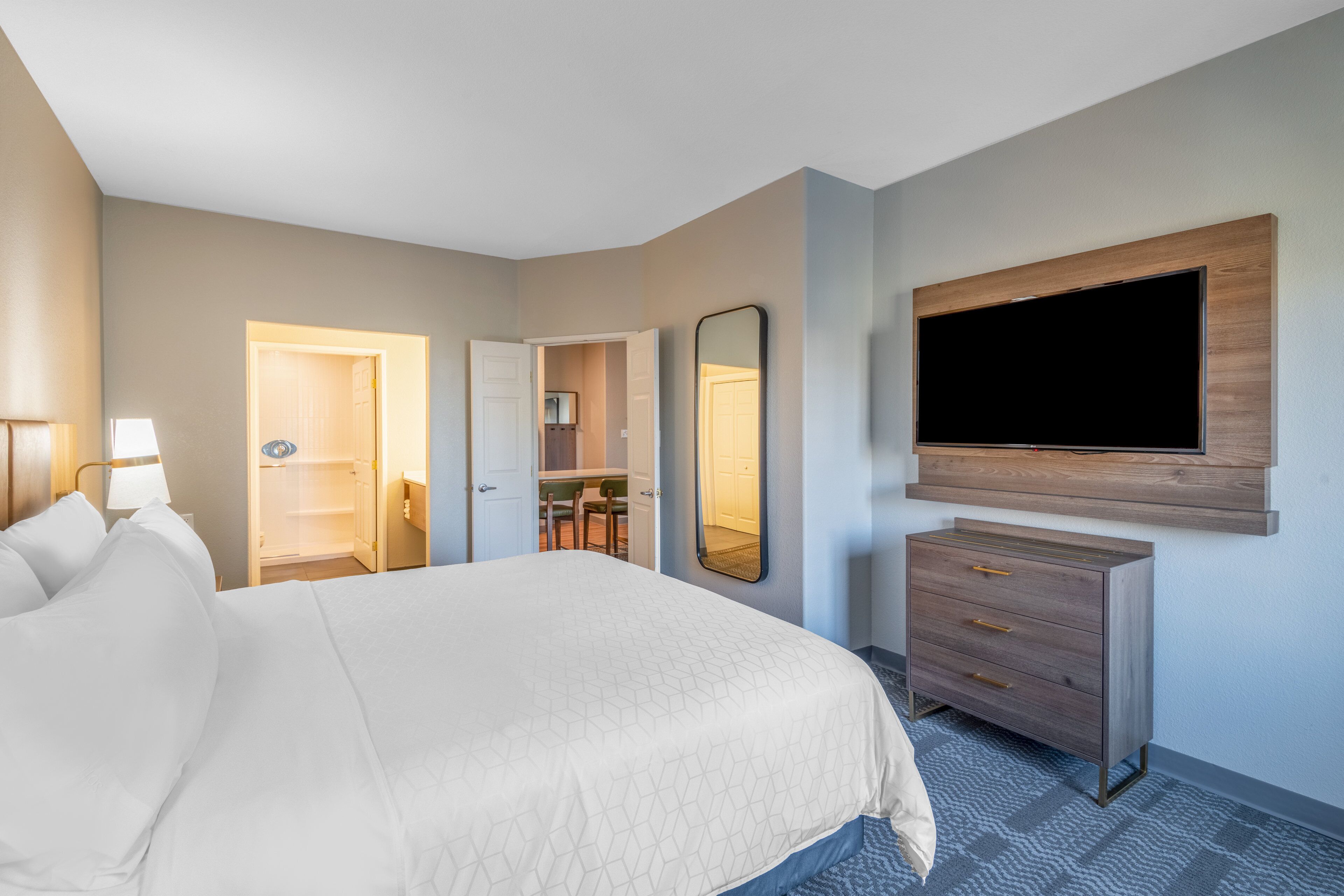 A hotel room with a large bed, a TV mounted on the wall, a dresser, and a mirror.