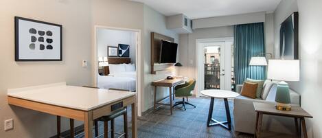 A hotel room with a bed, a desk, a chair, a table, and a TV.