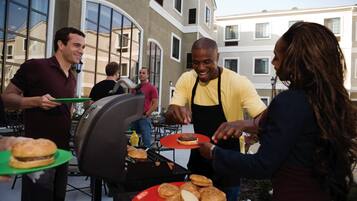 A group of people grilling food outdoors with a building in the background.